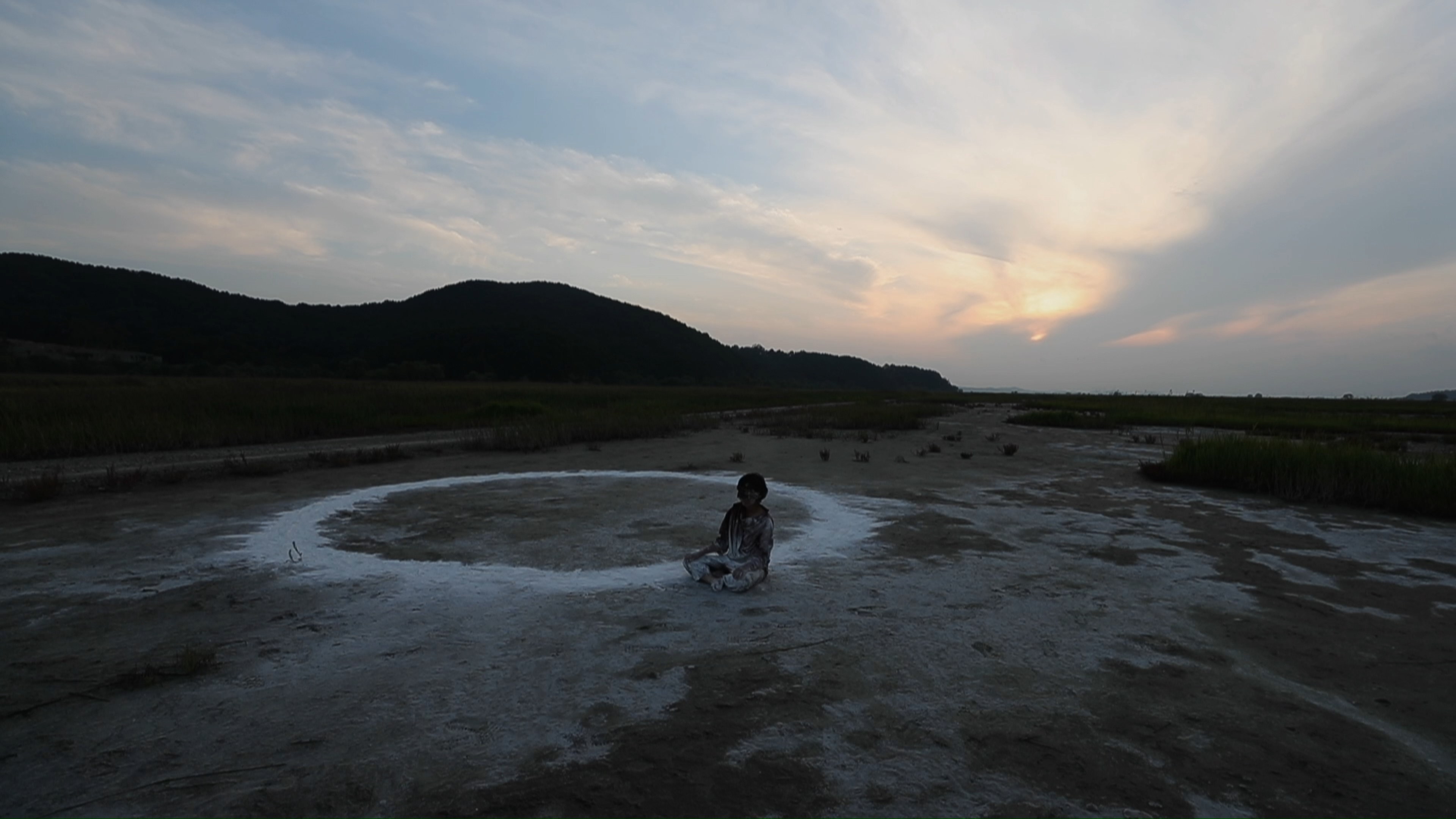 The performer seated inside the circle as daylight fades